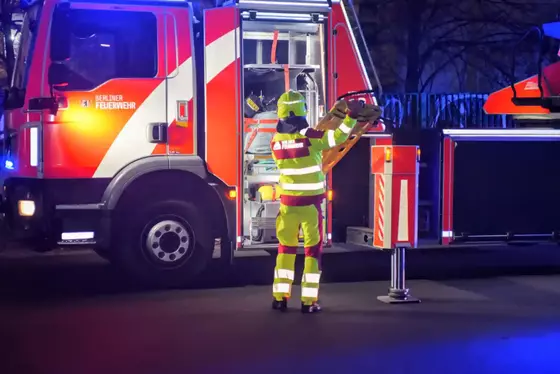 Einsatzkraft der Berliner Feuerwehr in reflektierender Schutzkleidung entnimmt ein Spineboard aus einem Einsatzfahrzeug bei Nacht