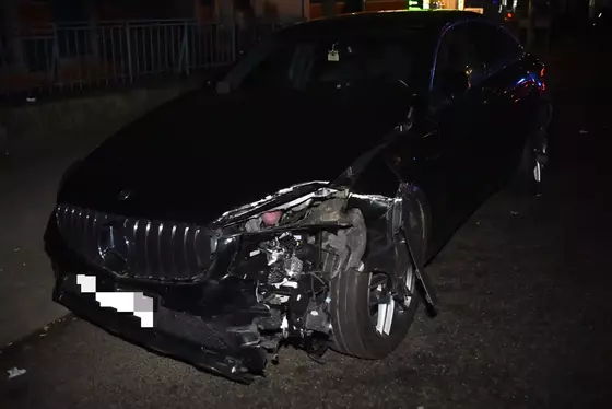 Schwarzer Mercedes-Benz mit erheblichen Frontschäden, insbesondere an der linken Fahrzeugseite, geparkt auf dunkler Straße bei Nacht