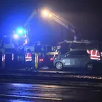 PKW wird nachts von Kranfahrzeug mit Blaulicht aus Gleisbett gehoben, mehrere Personen in Warnwesten stehen daneben