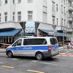 Polizeiwagen steht vor einem Eckgebäude mit blauem Markisen, das den Shisha-Club "Hook-Bar" zeigt, Straßensperrungen und Fahrräder sind sichtbar.