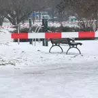 Schneebedeckter Park mit einer Bank und rot-weißem Absperrband im Vordergrund. An einer Stelle blutgetränkter Schnee.
