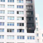 Fassade eines mehrstöckigen Gebäudes mit einer stark verrußten, schwarzen Fensteröffnung und mehreren intakten Fenstern