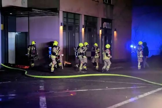 Feuerwehrleute mit gelben Helmen tragen ein bewusstloses Kind aus einem Hochhaus bei Nacht
