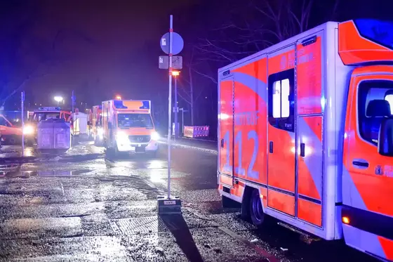 Mehrere Rettungswagen mit eingeschalteten Blaulichtern stehen nachts auf einer nassen Straße, im Vordergrund ein Rettungswagen mit der Nummer '112'