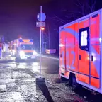 Mehrere Rettungswagen mit eingeschalteten Blaulichtern stehen nachts auf einer nassen Straße, im Vordergrund ein Rettungswagen mit der Nummer '112'