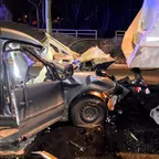 Schwarzes Auto mit schwer beschädigter Front nach Auffahrunfall auf einem grauen Auflieger bei Nacht