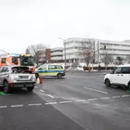 Zwei beschädigte Fahrzeuge an einer Kreuzung mit Feuerwehrleuten, einem Feuerwehrfahrzeug und einem Polizeiauto im Hintergrund