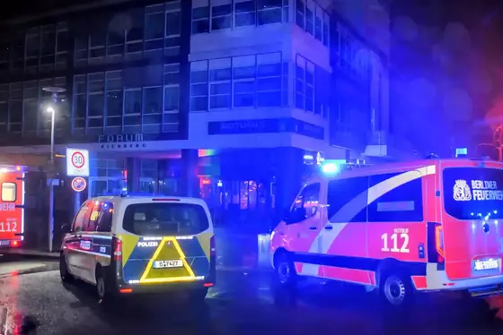 Drei Einsatzfahrzeuge von Polizei und Feuerwehr mit Blaulicht vor einem mehrstöckigen Gebäude bei Nacht