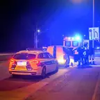 Polizeiauto mit eingeschaltetem Blaulicht steht nachts auf einer Straße hinter einem weißen Kleintransporter, mehrere Personen stehen daneben