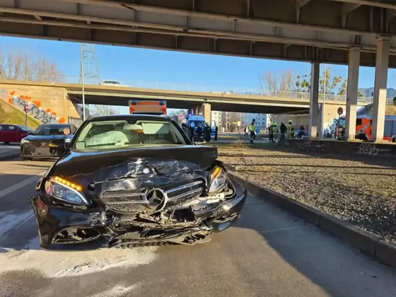 Schwarzes Mercedes-Auto mit stark beschädigter Frontpartie steht auf einer Straße unter einer Brücke, im Hintergrund Einsatzfahrzeuge und Personen