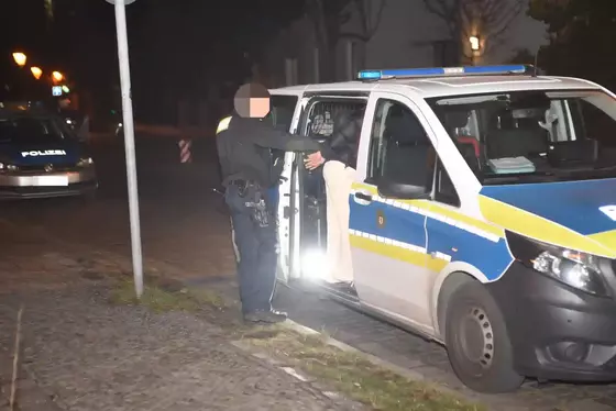 Polizist führt eine festgenommene Person in ein Polizeifahrzeug bei Nacht.