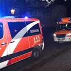 Zwei Rettungsfahrzeuge mit Blaulicht stehen nachts auf einer Straße vor dunklen Häusern.