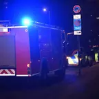 Rückansicht eines Einsatzfahrzeugs der Feuerwehr mit eingeschaltetem Blaulicht und einem Polizeiauto bei Nacht auf einer Straße.