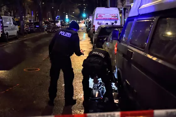 Zwei Polizisten sichern nachts an einer Straße Spuren an einem Fahrrad neben parkenden Autos.