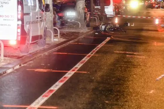 Nachtaufnahme einer Unfallstelle mit einem auf der Straße liegenden Motorrad, mehreren geparkten Fahrzeugen am Straßenrand und Markierungen auf der Fahrbahn zur Unfallaufnahme.