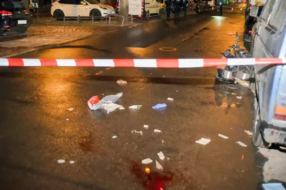 Absperrband vor einer nassen Straße mit verstreuten Gegenständen und einem kaputten Fahrrad neben einem geparkten Fahrzeug.