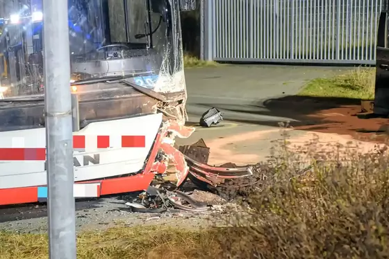 Vorderer Bereich eines beschädigten Busses mit zerbrochenem Frontstoßfänger und verstreuten Trümmern auf der Straße.
