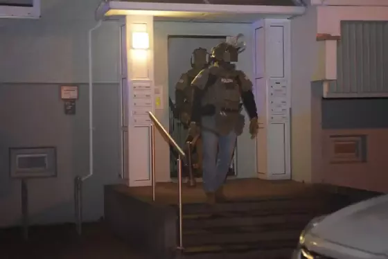 Zwei Polizisten in Schutzkleidung treten aus einem beleuchteten Hauseingang heraus.