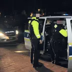 Zwei Polizisten in reflektierenden Westen setzen eine Person bei Nacht in ein Polizeiauto mit geöffneter Tür.