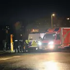 Mehrere Personen stehen nachts neben einem Einsatzfahrzeug mit eingeschaltetem Scheinwerfer auf einer Straße in einer Wohngegend.