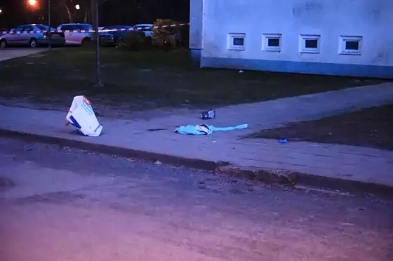 Tatort mit blutverschmierter Textilie und Einkaufstüte vor einem mehrstöckigen Wohnhaus.